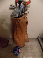 Full view of brown leather golf bag holding golf clubs with mixed heads including irons and drivers.