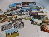 Photo showing a variety of 30 vintage postcards spread out on a white surface including color and black and white images, mostly city views and historic buildings.