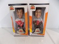 Both bobble heads in original packaging, viewed frontally showing clear plastic boxes and figure details.