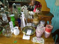 Photo showing assorted scented candles in jars, pillar candles, and various ceramic and glass vases arranged on a mirrored shelf with other decor items.