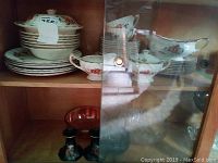 Shelf with stacked plates, serving bowls, and cups with floral pattern and gold trim.