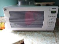 Closed view of Panasonic white microwave oven on countertop with muffin pan and splash guard on top
