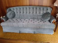 Full front view of the blue velvet tufted sofa including two round pillows