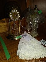 Two electric cut glass lamps, anniversary clock under glass dome, and crocheted doily on wood surface