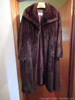 Front view of full-length dark brown fur coat on hanger against wooden door