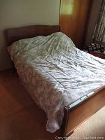 Double bed fully assembled with bedding on it, showing wooden headboard and footboard with mattress and box spring beneath the comforter.