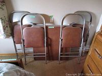 Five items: one card table with padded brown surface, four folding metal chairs with brown padded seats and backs.