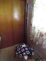 Wooden coat tree with four hooks, two afghan blankets and fleece blanket draped on foot stool in room corner near window with floral curtain.