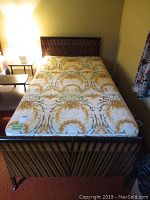 Full view of metal single bed with mattress on top showing floral pattern and metal frame.