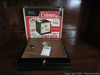 Vintage Coleman fold-up camp oven shown with original box. Oven top panel visible with temperature gauge and control knob.