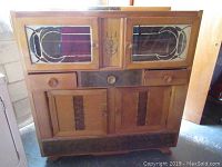 Front angled view of the wooden dining server cabinet showing upper glass panel doors with etched designs, middle drawers, and lower wooden doors with panels.