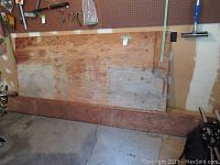 Plywood sheet and wood planks leaning against a wall in a garage/workshop setting