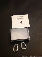 Photo showing pair of silver teardrop earrings next to a small box and auction card, displaying shape, size, and condition.