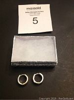 Pair of small .925 silver hoop earrings placed on a dark surface along with a small box underneath an auction number card.