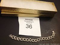 Silver bracelet laid out with textured gold-tone rectangular storage box beside it, photo shows full length and box.
