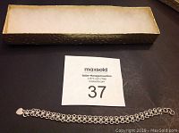 Image of the .925 silver wrist bracelet laid flat on a dark surface next to its storage box and auction tag.
