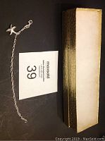 Silver wrist bracelet with starfish charm and lobster clasp on black background, accompanied by gold-toned box.