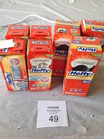Photo shows seven boxes of Hefty trash bags in assorted sizes and counts on a gray surface, including Small, Medium, and Tall Kitchen variants with some featuring Arm & Hammer scent.