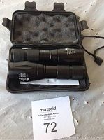 Two black expandable flashlights inside a black foam-padded carrying case, placed on a white surface with a MaxSold auction card number 72 visible.