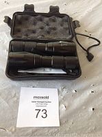 Two black expandable flashlights inside a black foam-padded carrying case, with instruction manual visible underneath.