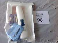 White electric pet nail grinder with blue power button, two AA batteries, blue cleaning cloth, original packaging and instruction manual visible within sealed plastic bag.