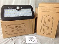 Two black Arilux solar sensor lights on packaging boxes showing front LED panel and motion sensor