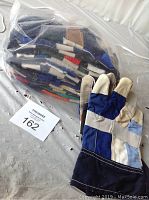 Photo shows a clear plastic bag with a dozen assorted large work gloves and one glove outside the bag displayed flat to show materials and colors.