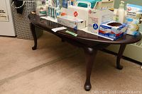 Wood coffee table with various medical and hygiene items placed on top; showing curved legs and dark wood finish.