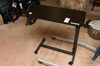 Full view of the bedside hospital bed table showing dark wood-grain tabletop and black metal base with casters under the table.