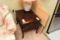 Side angle view of Gibbard solid mahogany side table with drawer next to floral sofa and wooden board against wall.