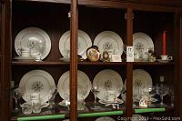 View of two shelves inside wooden buffet cabinet featuring eight place settings of Bavaria china, crystal glassware, and decorative porcelain items including Limoges egg.