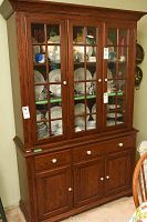 Full front view of the Almira solid wood china cabinet showing its four glass-paned doors on upper section, wooden base with drawers and doors, and white round knobs.