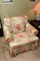 Front and angled view of floral upholstered armchair with cushioned seat, back and arms, showing pleated skirt on base.