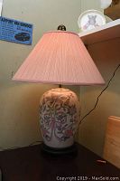 Front view of ceramic floral painted table lamp with pink pleated fabric shade on a dark base