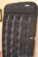 Full view of the black inflatable air mattress in folded/wrapped state showing tufted surface and inflation valve.