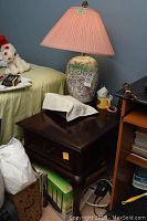 Side view of the solid mahogany table with one ceramic floral lamp with pink shade on top, showing drawer detail and surrounding clutter.