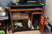 Front view of pressed board computer table showing keyboard tray, shelving with stacks of papers, and lower cabinet space partially open with visible items underneath (not included in sale).