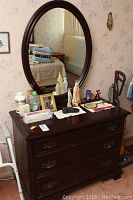 Front view of solid mahogany dresser with attached oval mirror and assorted items on top