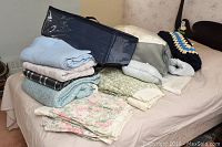 Collection of folded linens including blankets, comforters, tablecloths, and pillow shams laid out on a bed.