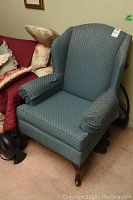 Front and side view of an upholstered wing back chair with blue-green patterned fabric, showing the full chair including cushioned arms and backrest.