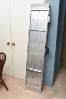 Full view of folded aluminum portable ramp leaning against wall.