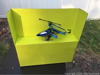 Blue and silver Protocol Turbohawk drone with dual rotor blades and tail rotor sitting on yellow box outdoors
