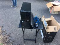HP 110 black desktop tower with keyboard, mouse, blue Ethernet cable on small black table. HP box visible beside the table.