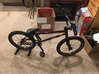 Full view of purple Kink Launch BMX bike with bike stand on carpeted floor, showing frame, seat, handlebars, pedals, and wheels.