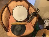 Full view of percussion lot on chair including snare drum, drumsticks, practice pad, and drum stand.