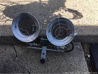 Photo showing front view of propane heater with two circular metal burner covers, protective grilles, and connected hose assembly.