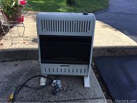 Front view of the beige Pro Com space heater showing ventilation slots, black flame viewing panel, base legs, and attached gas hose with valve.