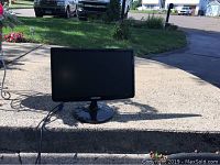 Front view of Samsung LED monitor on a round base stand outdoors, showing screen and cables attached.