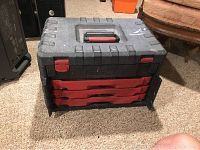 Closed Craftsman tool box showing black exterior with red latches and handle, and three red pull-out trays visible.