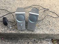 Front view of two Bose Companion 2 speakers side by side showing silver front panels and speaker grills, power adapter cable visible